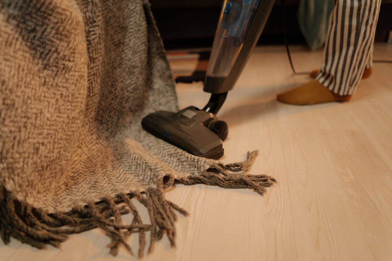 Close-up of vacuum cleaner cleaning a woolen blanket on the floor indoors.