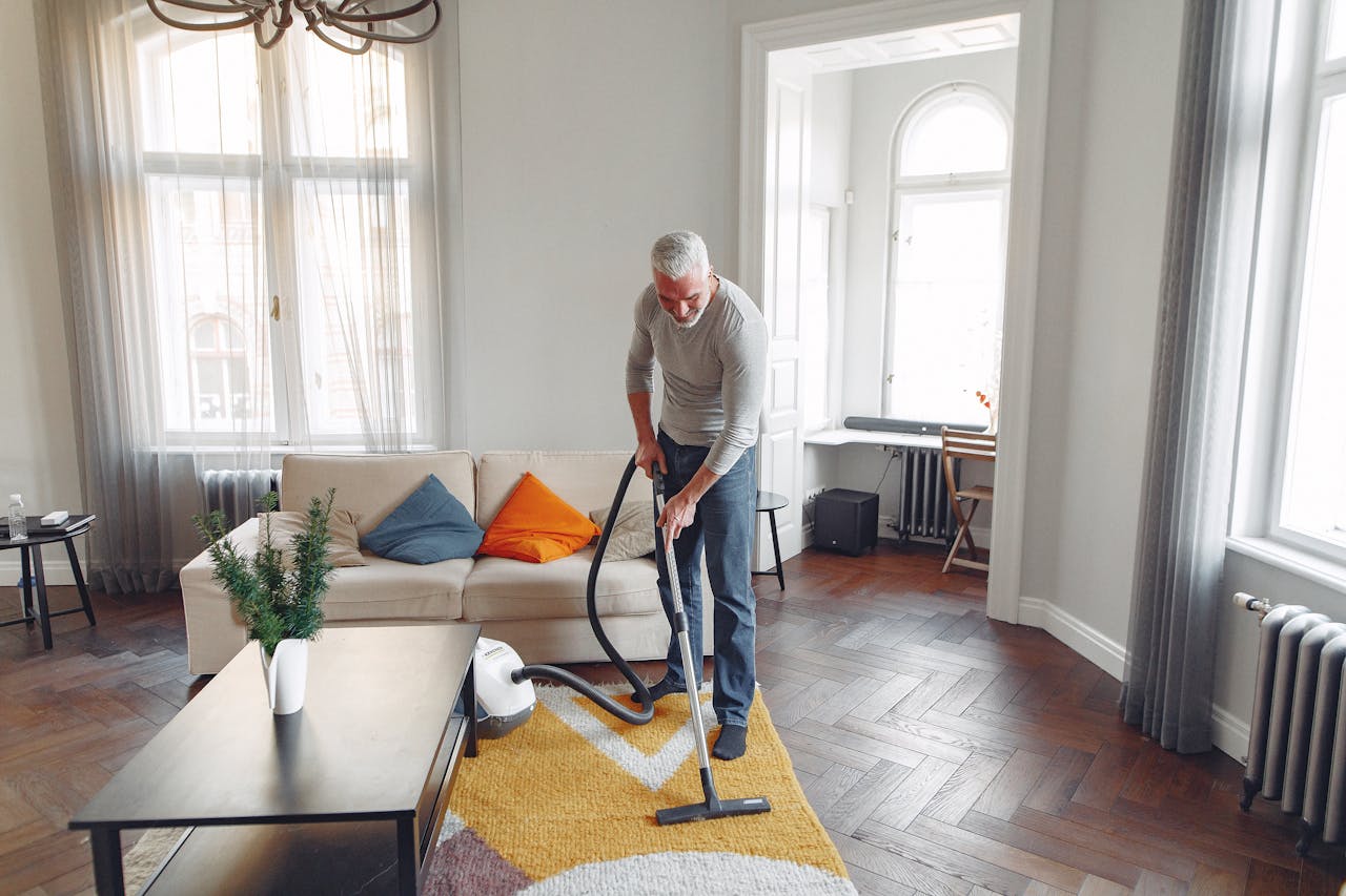 From above of focused grey haired man with beard vacuum cleaning carpet at home
